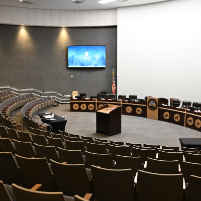 Interior of a government chamber, several rows of chairs curving around a podium which faces a row of chairs for officials and another podium. A screen is high on the wall above the chairs for officials.