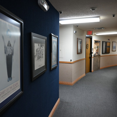 Gently curving hallway with a gray carpet and blue walls, on which is displayed several framed art pieces and photographs.